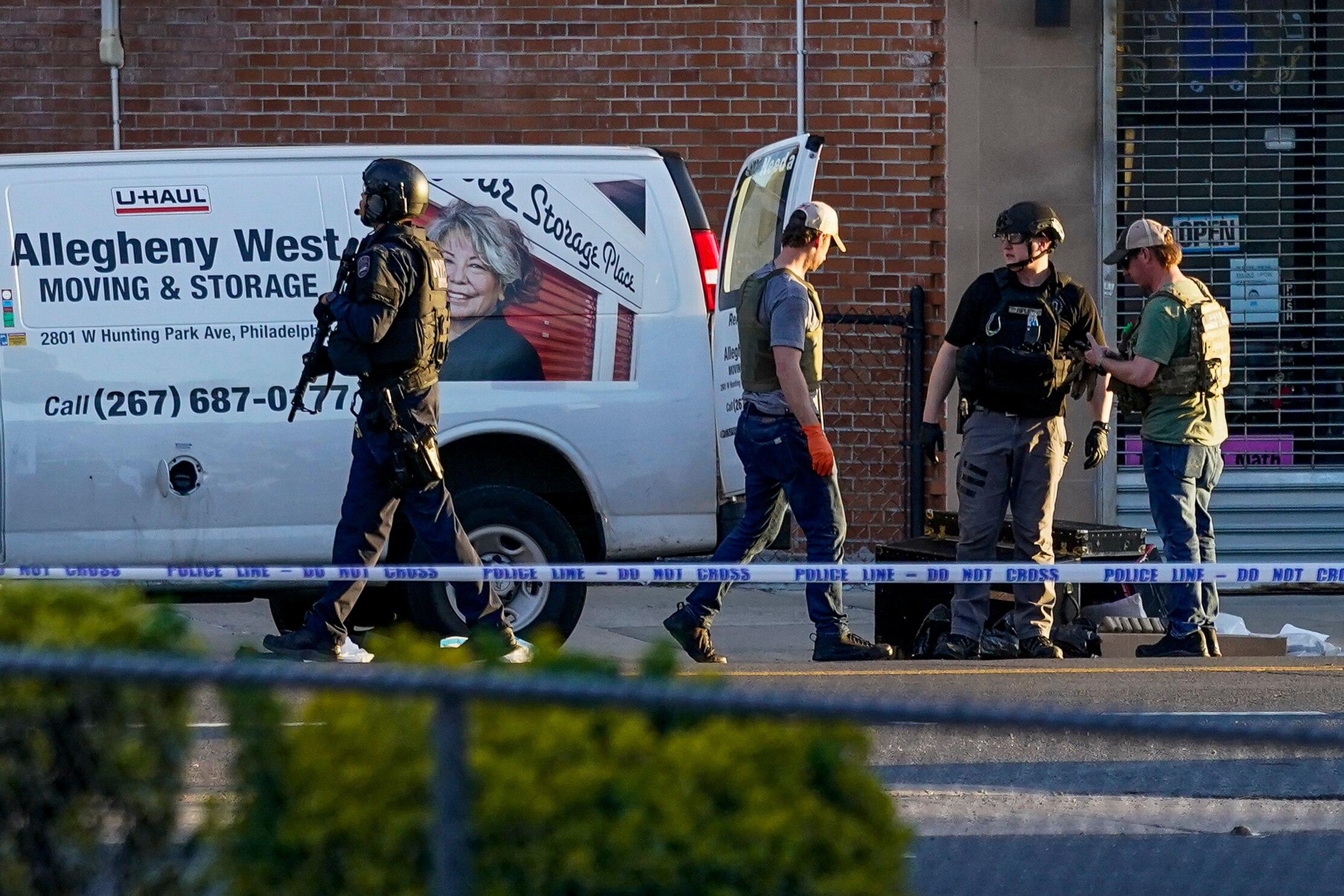 Police with guns and helmets stand near a white van