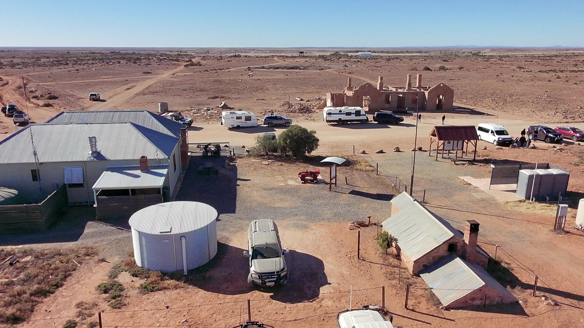 A drone image of a few buildings and ruins in a red dirt outback settlement.