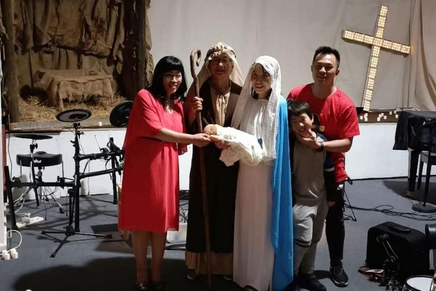 Two people dressed in costume for a nativity performance stand on a stage with two other smiling adults.