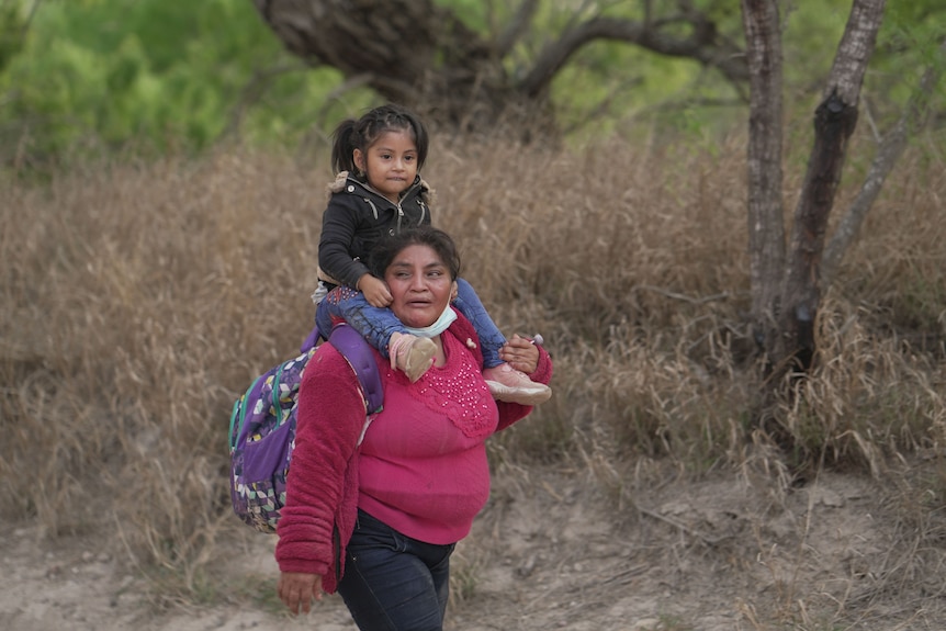 A woman walks with a young girl sitting on her shoulders.
