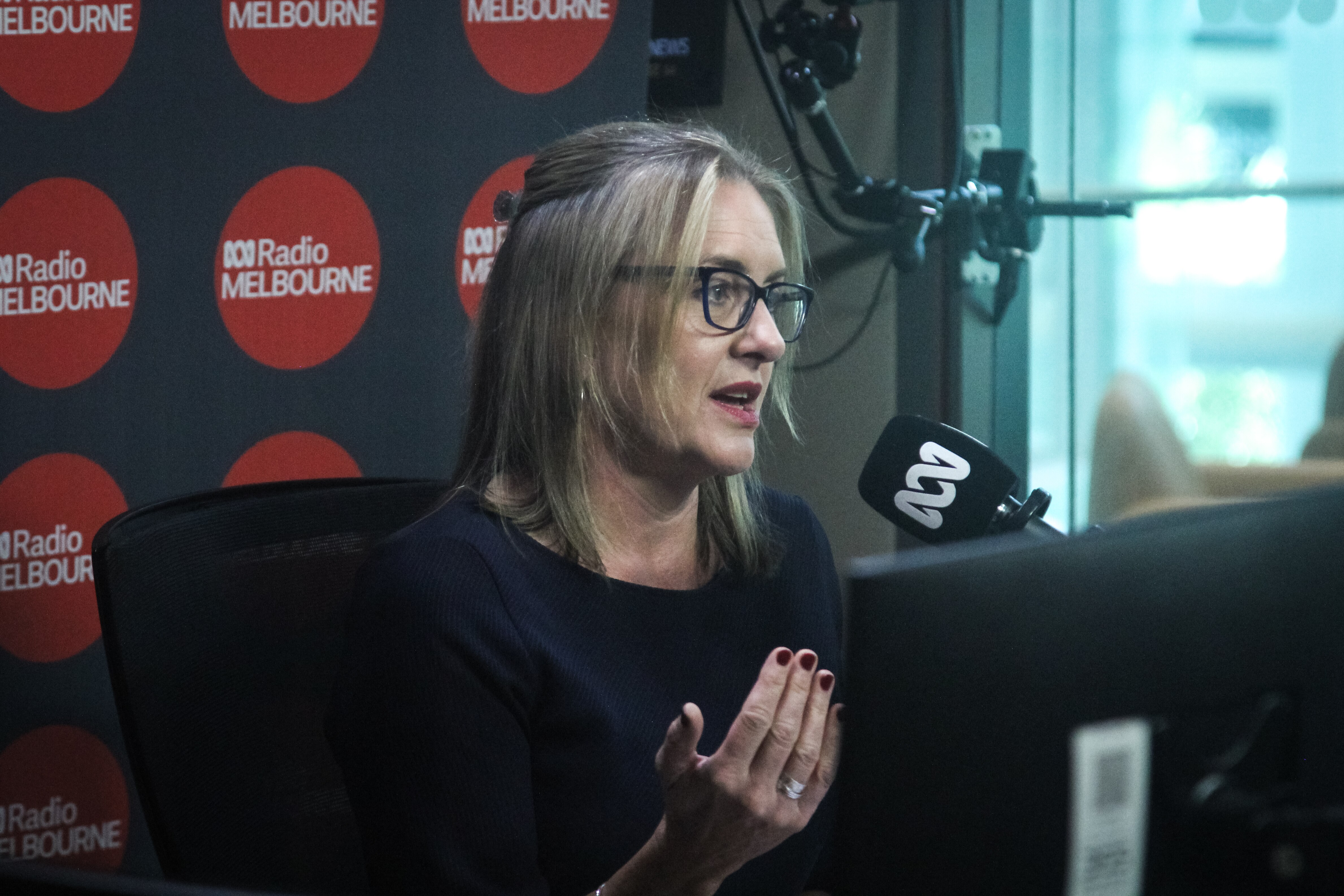 A blonde woman wearing glasses speaks into an ABC-branded microphone.