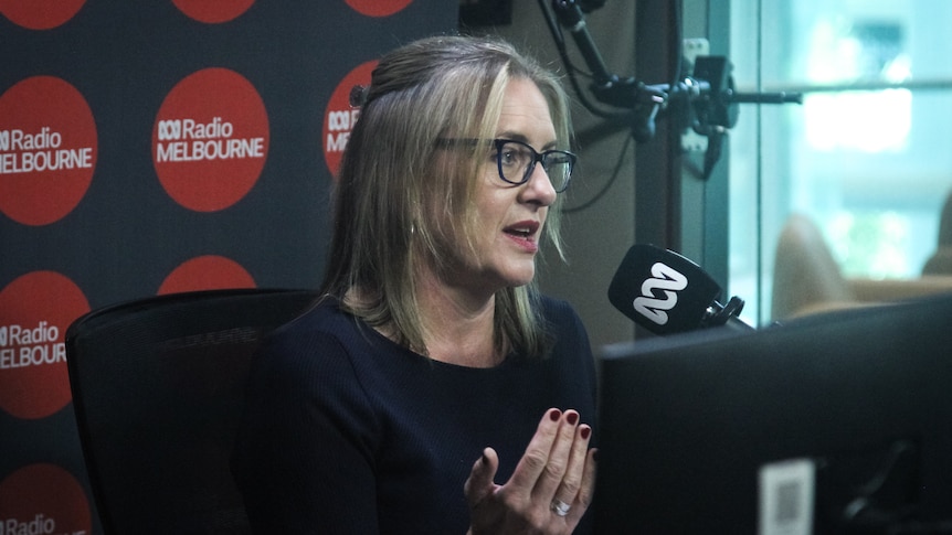 A blonde woman wearing glasses speaks into an ABC-branded microphone.
