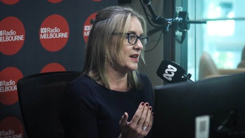A blonde woman wearing glasses speaks into an ABC-branded microphone.