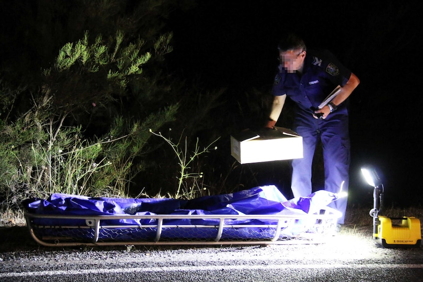 A police crouches over a body bag at Second Valley.