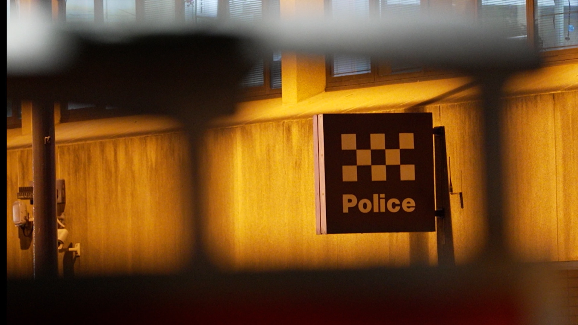 A police sign with the checker symbol of police on the side of a building at night.