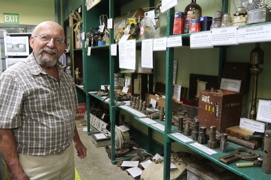An older man with glasses stands next to labelled artefacts