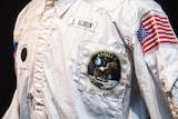 A white jacket with a collar, an Apollo 11 emblem with an eagle on it and a United States flag.  
