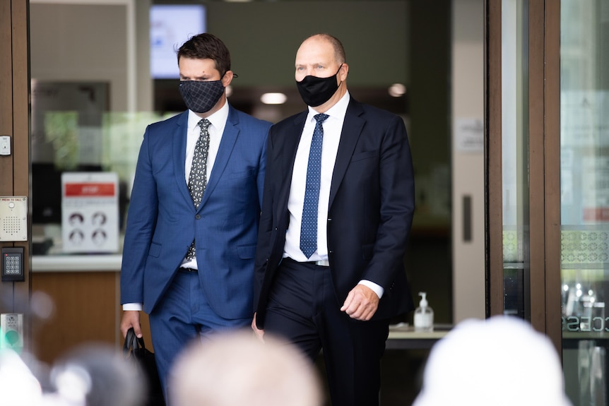 Two men in suits wearing face masks walking out of a building.