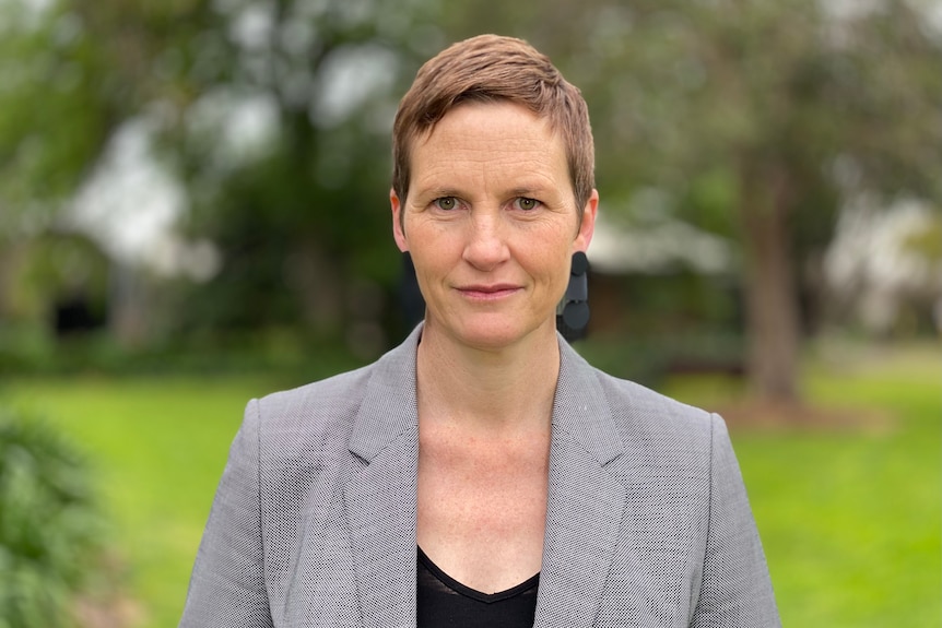 A woman in a grey suit looks into the camera.