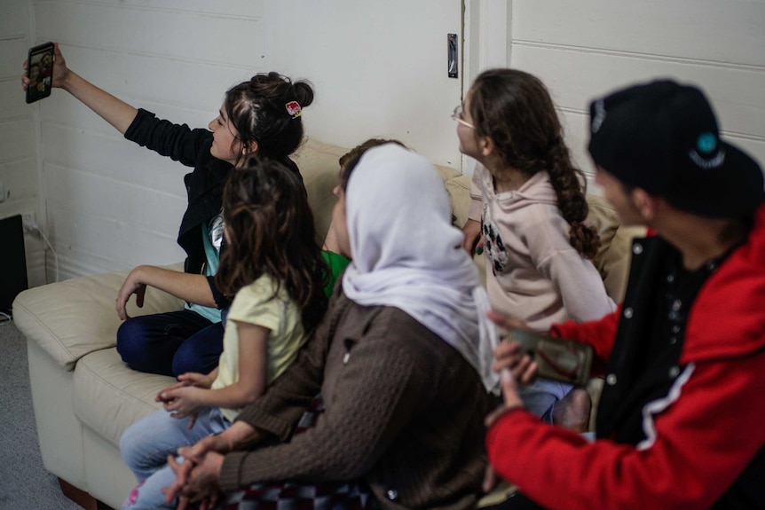 A family gathers around a phone to video chat with their family member.