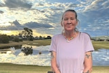 Emma Bates smiles, standing in front of a body of water under a sunny sky dotted with clouds.