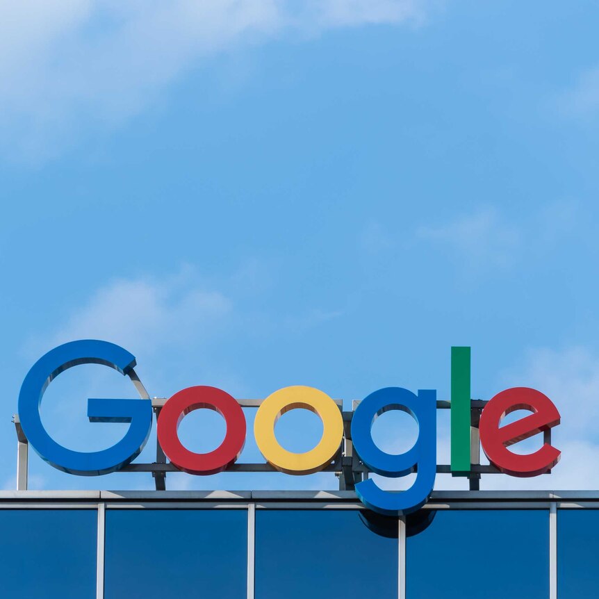 The logo for Google, brightly coloured letters spelling out the company name, sits atop a building against a bright blue sky.
