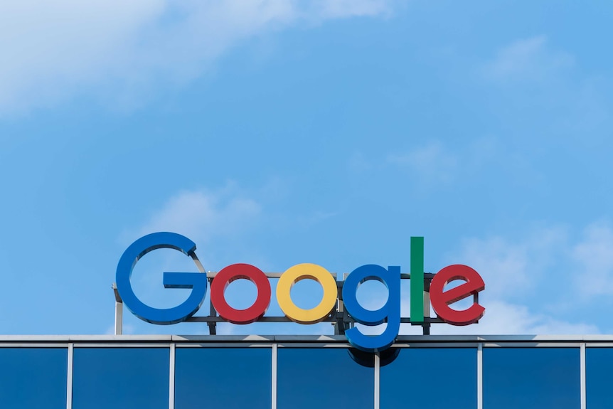 The logo for Google, brightly coloured letters spelling out the company name, sits atop a building against a bright blue sky.