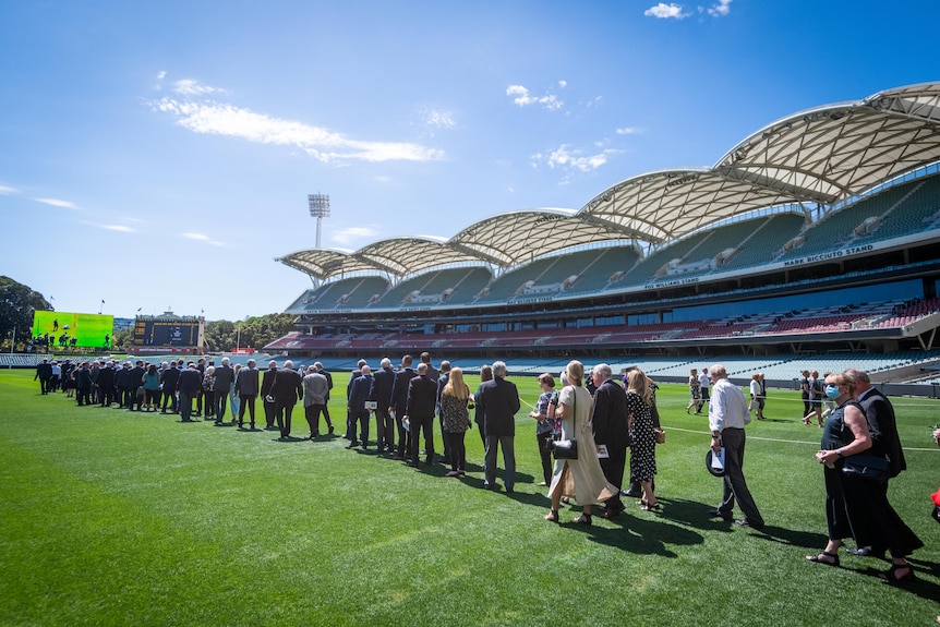 A procession of people walk out onto Adelaide Oval to pay respects to Rod Marsh after his service.