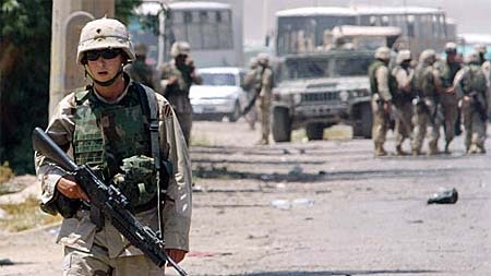 A US soldier patrols a Baghdad road where a Humvee vehicle was destroyed in an attack.