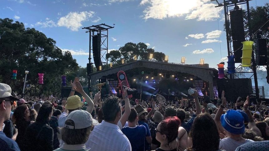 A crowd gathers in front of a stage at a music festival on a sunny day