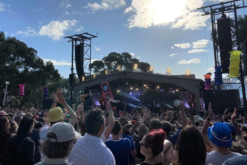 A crowd gathers in front of a stage at a music festival on a sunny day