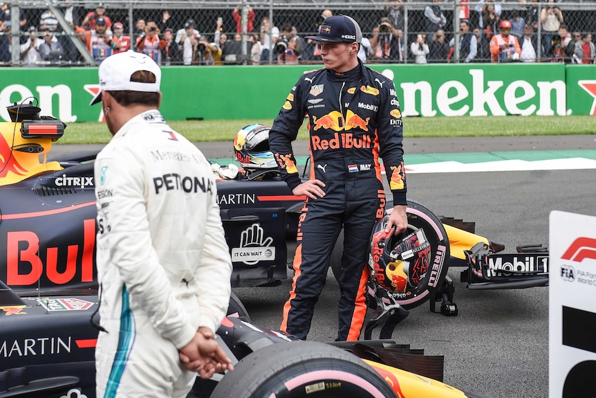 Formula One driver Max Verstappen has a sour look on his face as he stands next to his car on a race track.