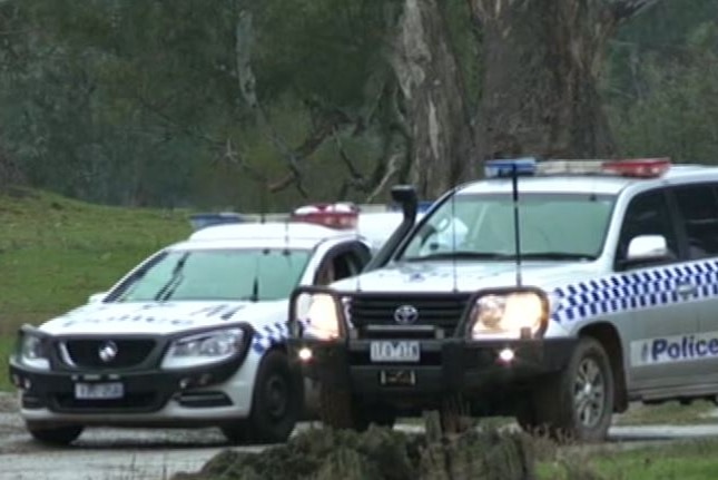 Two police cars in a green, rural setting with trees in the background.
