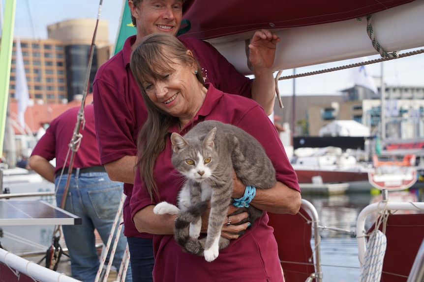 A woman holds up a cat on the deck of a yacht.