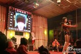 A stripper is on stage in front of a screen with a photo of the deceased.