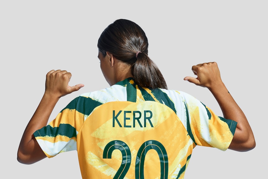 Sam Kerr points her thumbs at her back, which has her name and number, 20, displayed