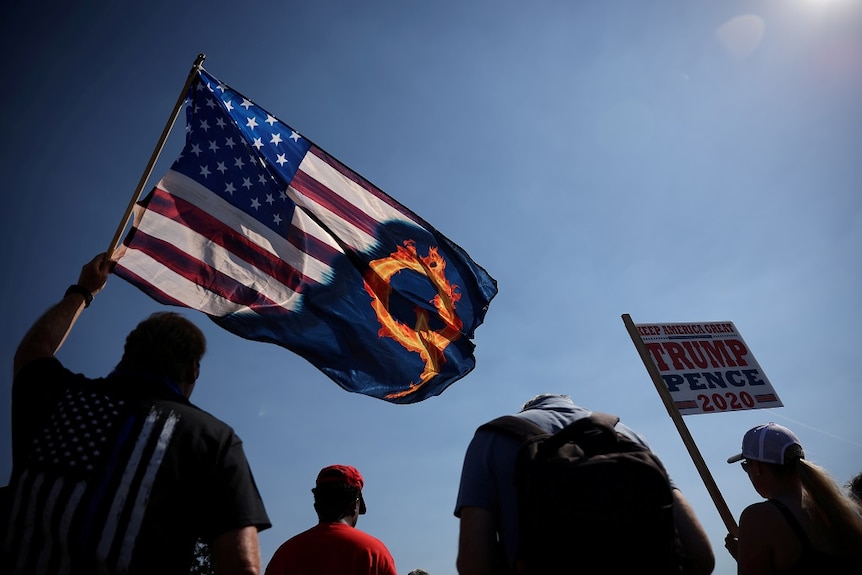 A supporter of President Donald Trump holds a US flag with a reference to QAnon during a Trump 2020 Labor Day cruise rally.