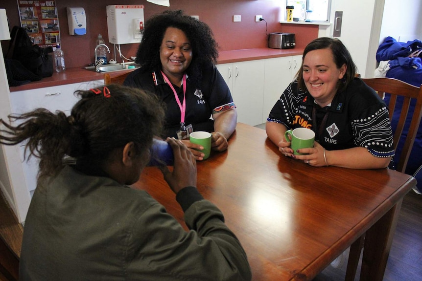 Two women sit at a table speaking with a young Indigenous woman.