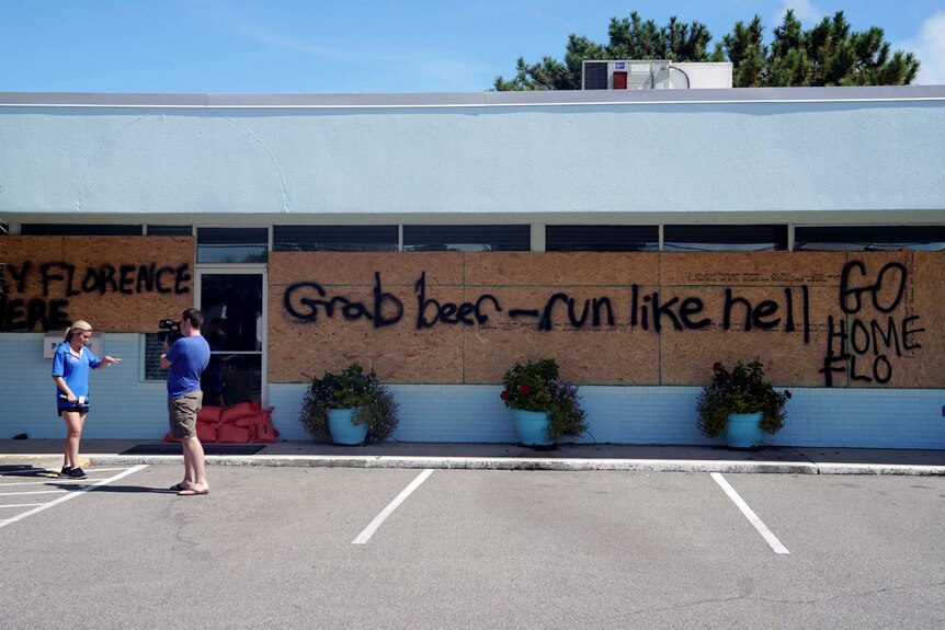 Graffiti says 'Grab beer — run like hell' on a boarded up shop as a reporter and cameraman stand outside
