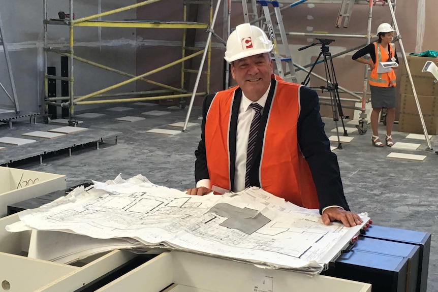 Member for Wagga Wagga, Daryl Maguire, wears a high-viz vest and hard hat looking at plans for the new Wagga Courthouse complex