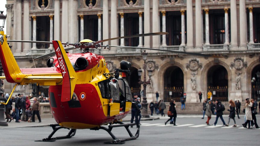 A yellow and red helicopter is parked in the middle of Paris's Place de l'Opera in front of the Palais Garnier
