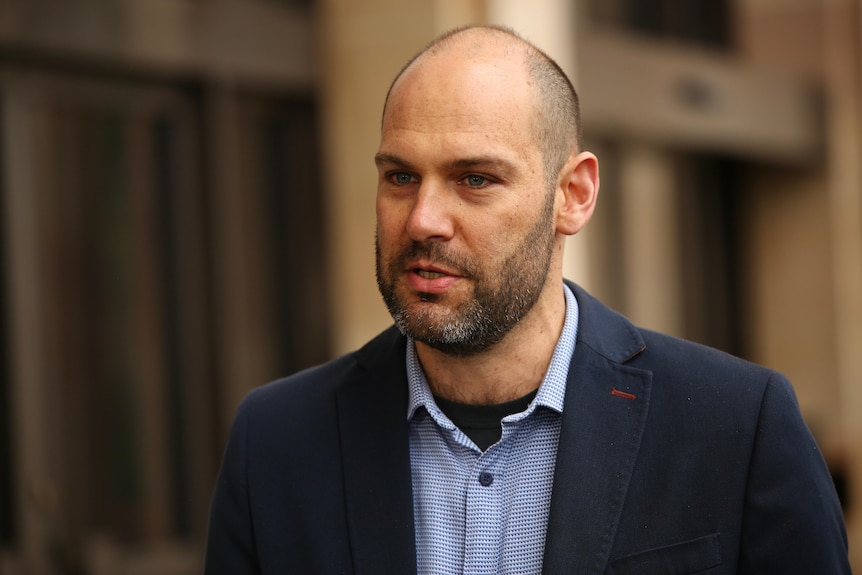 A bald man speaks at a press conference