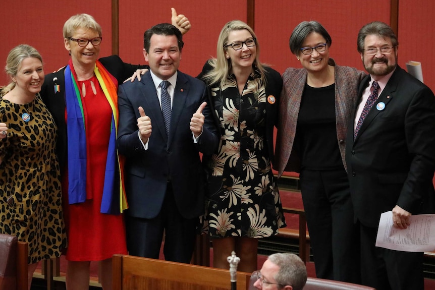 Liberal Senator Dean Smith smiles and gives a thumbs up as fellow Senators surround him.
