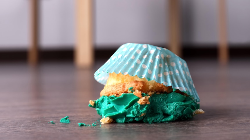 A cupcake with green icing, upside down and a bit smashed, on the floor