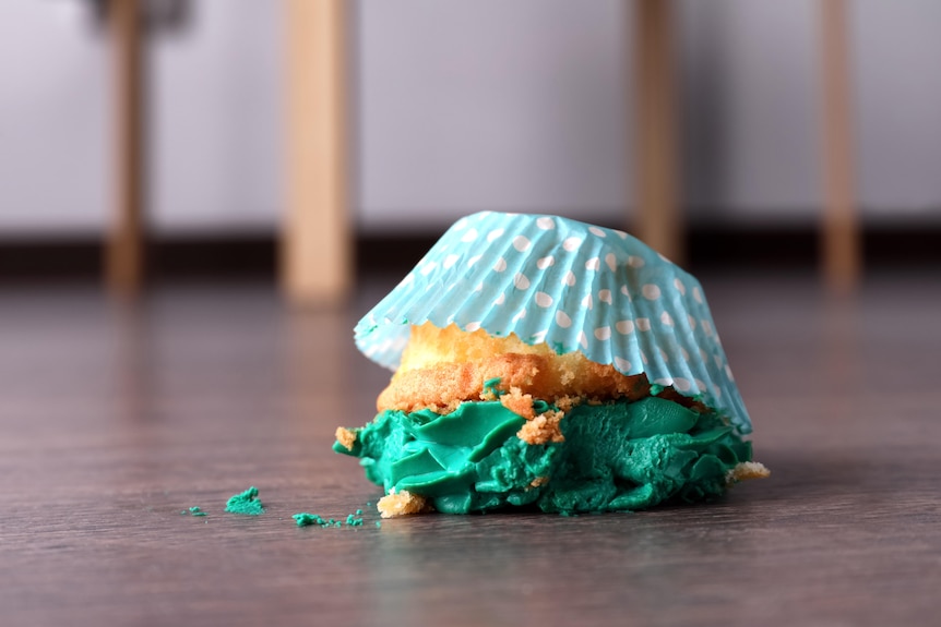 A cupcake with green icing, upside down and a bit smashed, on the floor