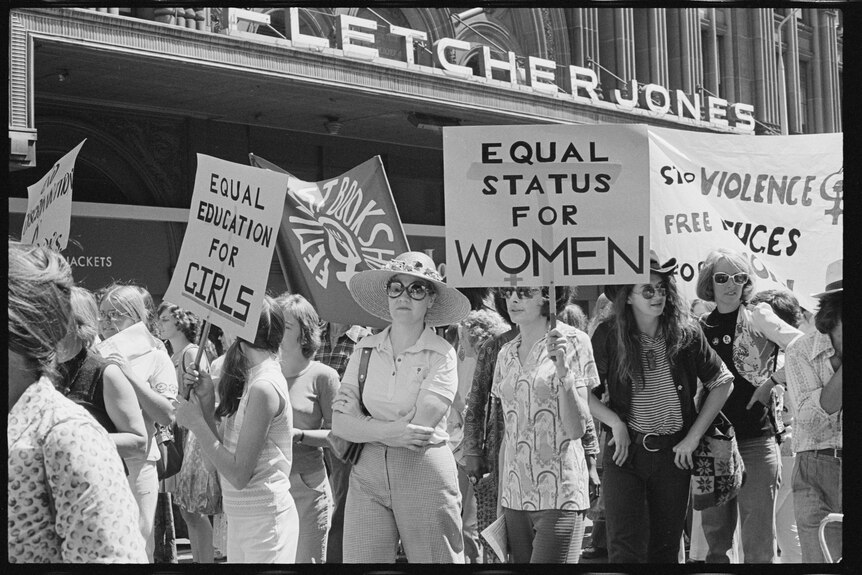 Black and white picture of women protesting under signs saying 'Equal Status for Women' 