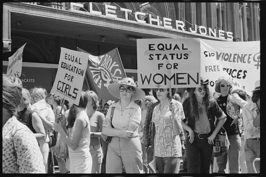 Black and white picture of women protesting under signs saying 'Equal Status for Women' 