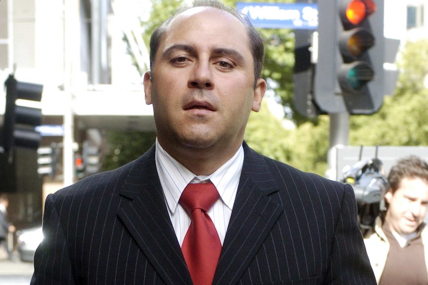 Tony Mokbel dressed ina black suit and red tie for a court hearing looks directly at the camera.