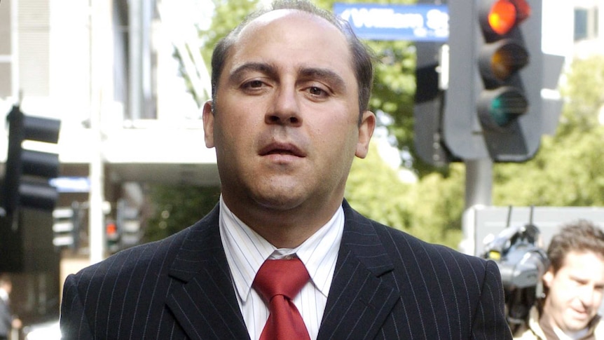 Tony Mokbel dressed ina black suit and red tie for a court hearing looks directly at the camera.