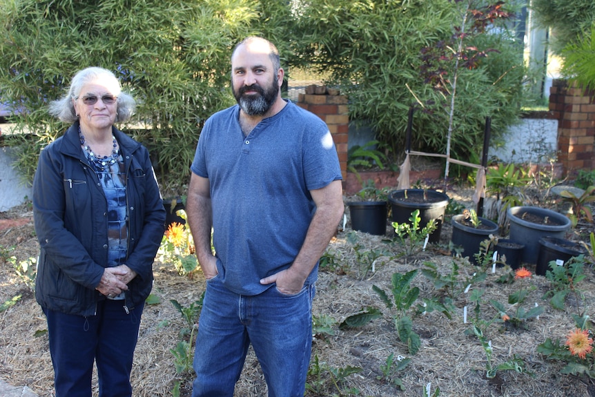 An old woman and a man with a beard smile in front of the garden