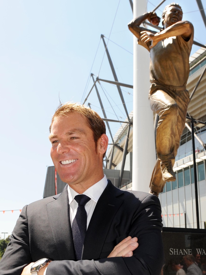 Shane Warne poses for a photo in front of a bronze statue of himself at the MCG.