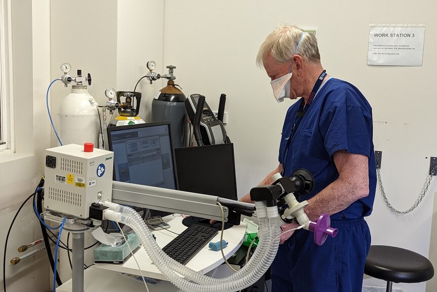 Associate Professor Lou Irving stands looking at a lung function monitor