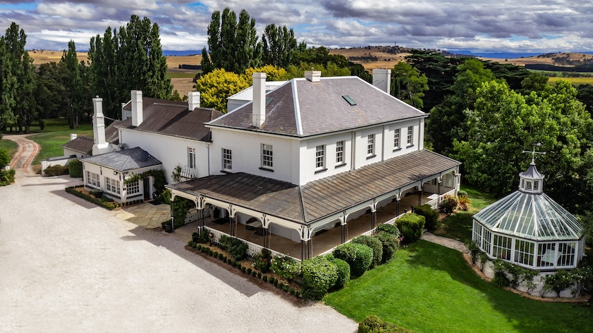 A large, white, Georgian era homestead sits among manicured lawns and trees. 