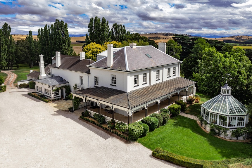 A large, white, Georgian era homestead sits among manicured lawns and trees. 