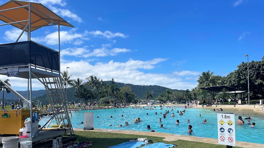 A swimming lagoon with dozens of people in it, and a lifeguard tower to the left of the shot.