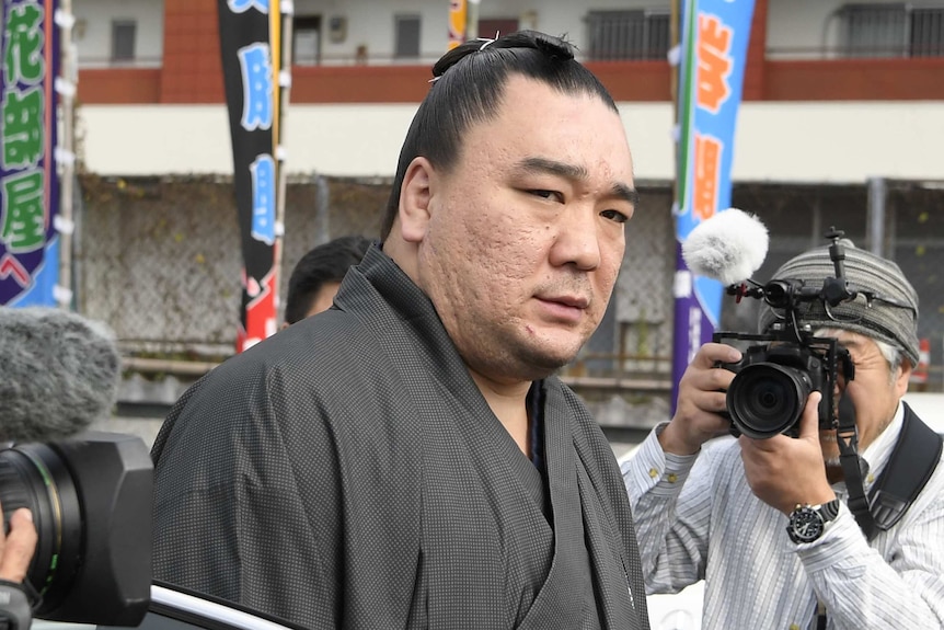 Sumo wrestler Harumafuji looks at the camera while surrounded by a number of other photographers.