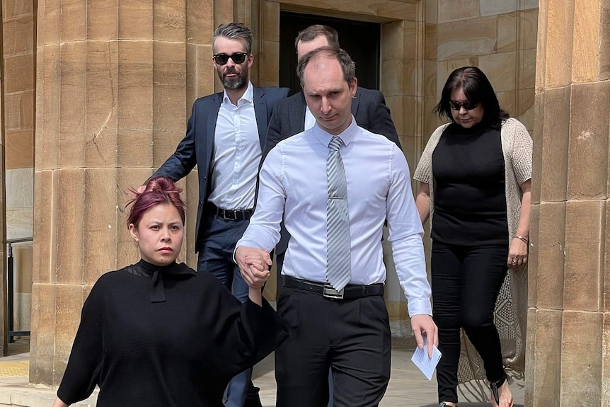 A man wearing a shirt, tie and trousers walks down the stairs at the front of a court building.