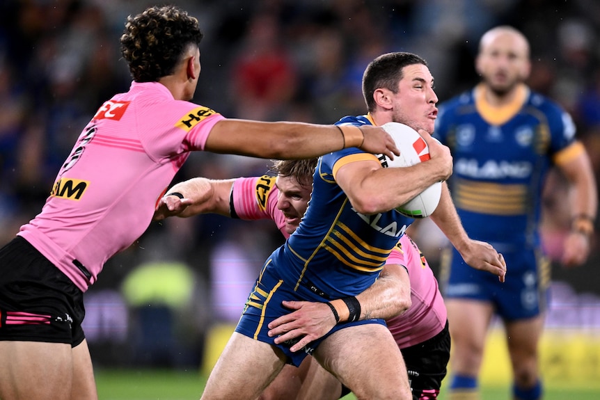 A Parramatta Eels NRL player holds the ball as he is tackled by the Penrith Panthers.