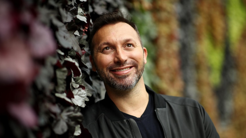 Ian Thorpe stands next to a wall of leaves.