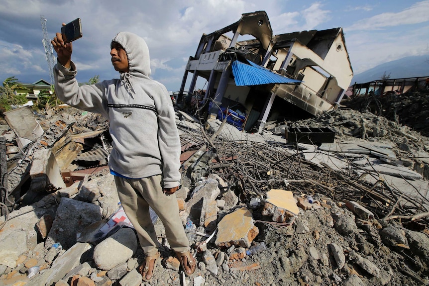A man takes pictures beside a toppled house
